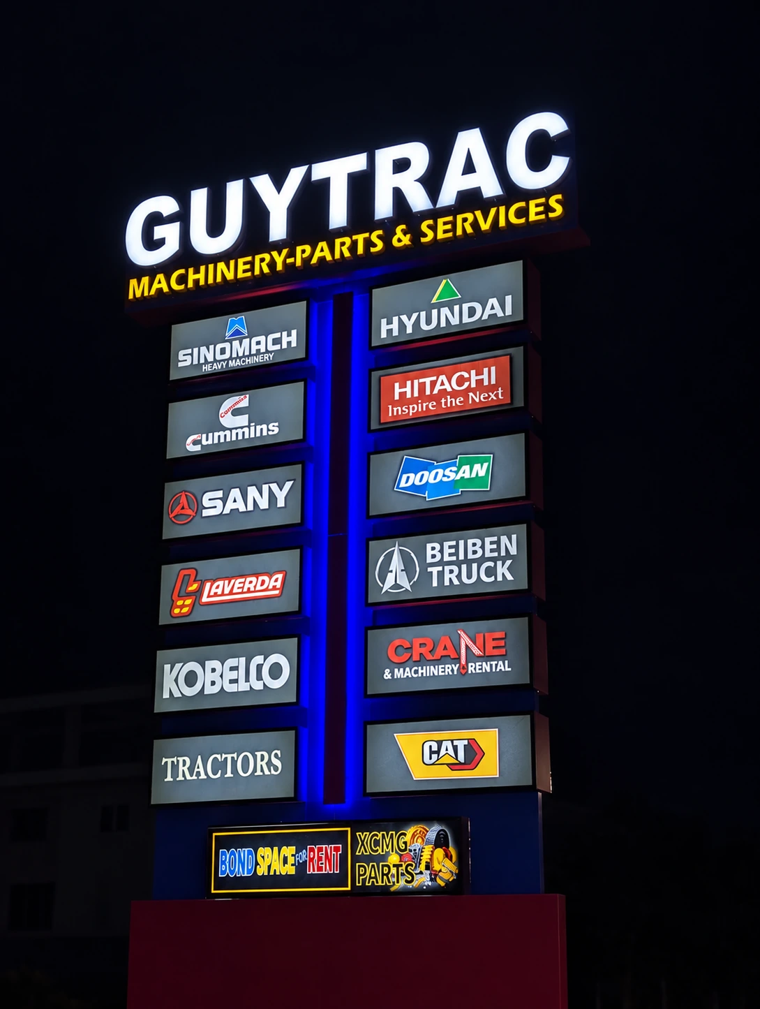 GUYTRAC illuminated machinery, parts and services directory sign with equipment-brand panels and blue lighting at night
